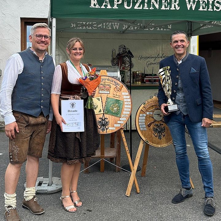 Eine Gruppe von drei Erwachsenen steht in zwei Reihen vor einem modernen Holzgebäude. In der vorderen Reihe stehen von links nach rechts Andreas Lorenz, Franziska Lorenz und Oliver Göckel. Alle Personen lächeln.